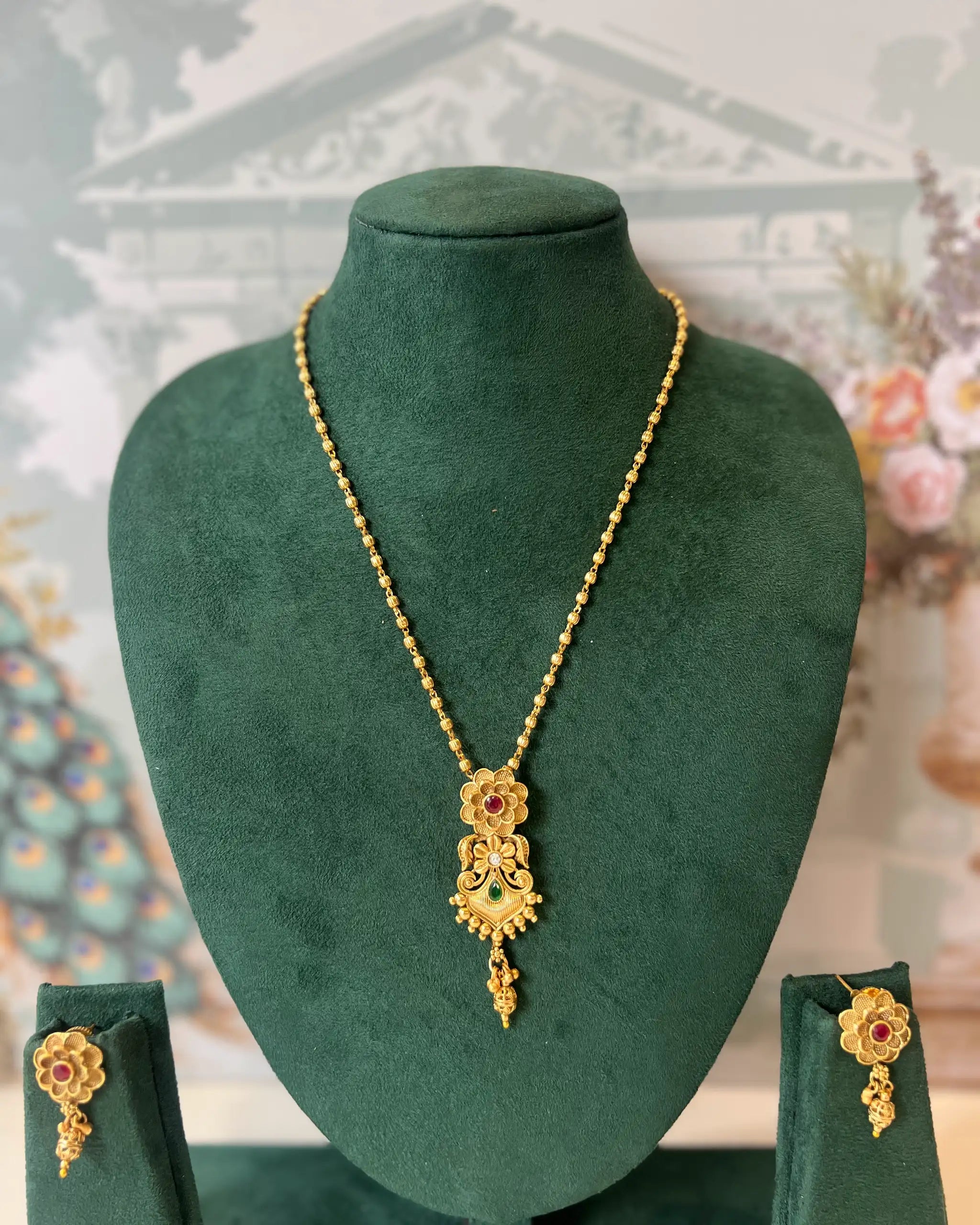 Gold necklace with floral pendant set with red and green stones, with matching drop earrings