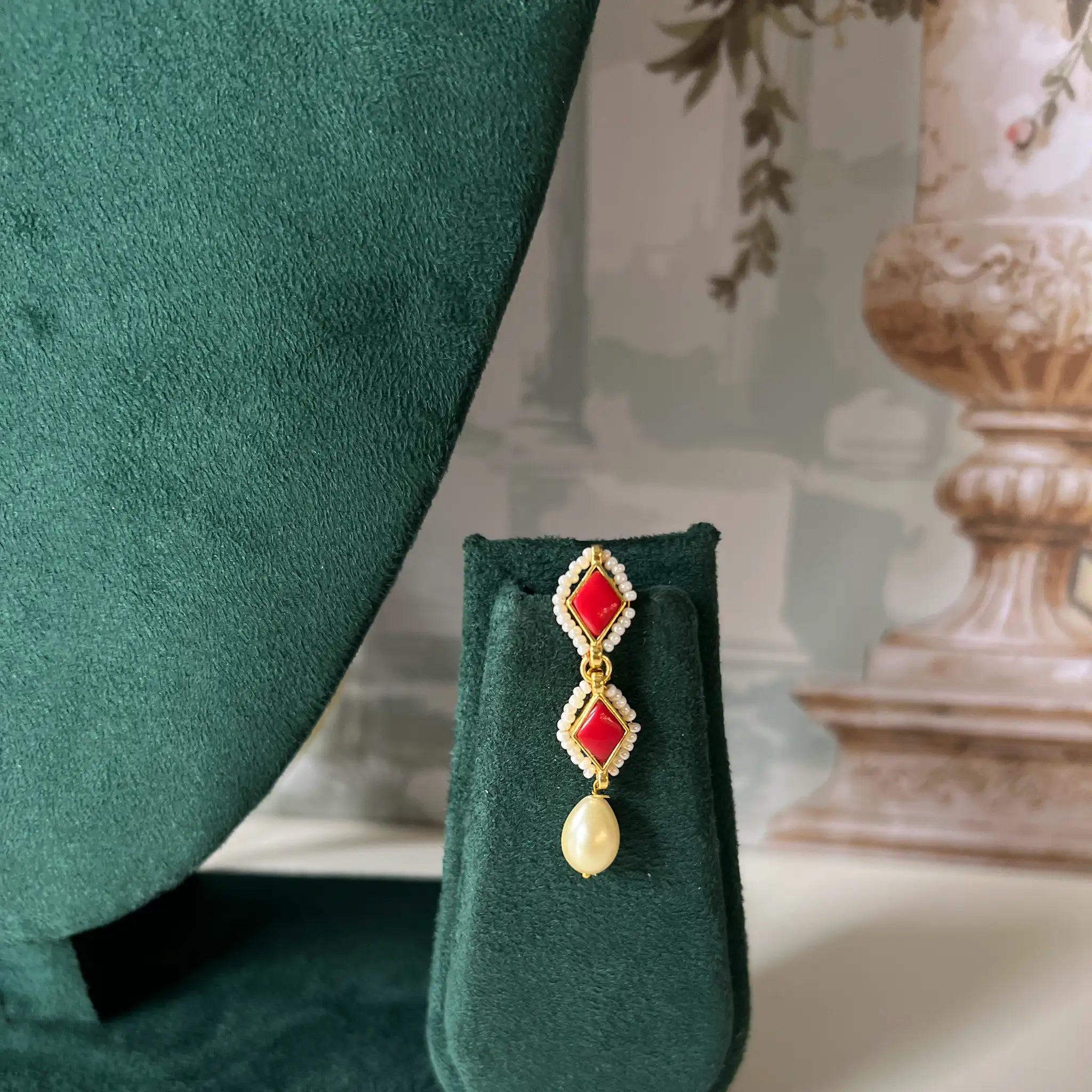 Close-up of drop earring with red stone and pearl detail