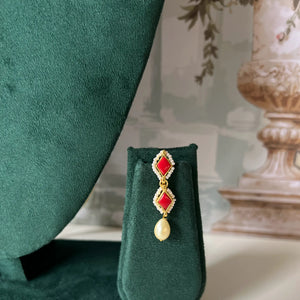 Close-up of drop earring with red stone and pearl detail