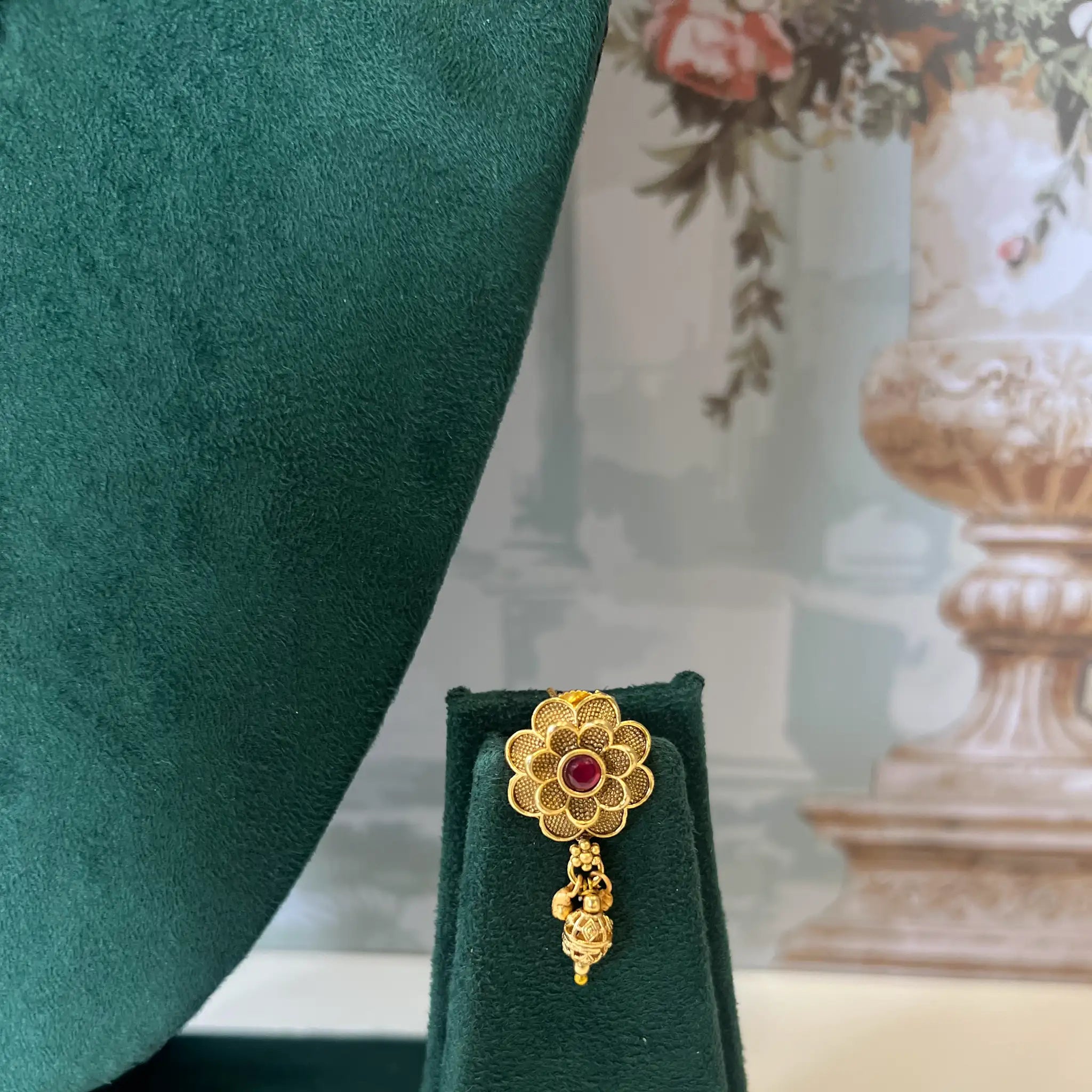 Close-up of gold filigree flower stud earring with ruby-red center stone and drop