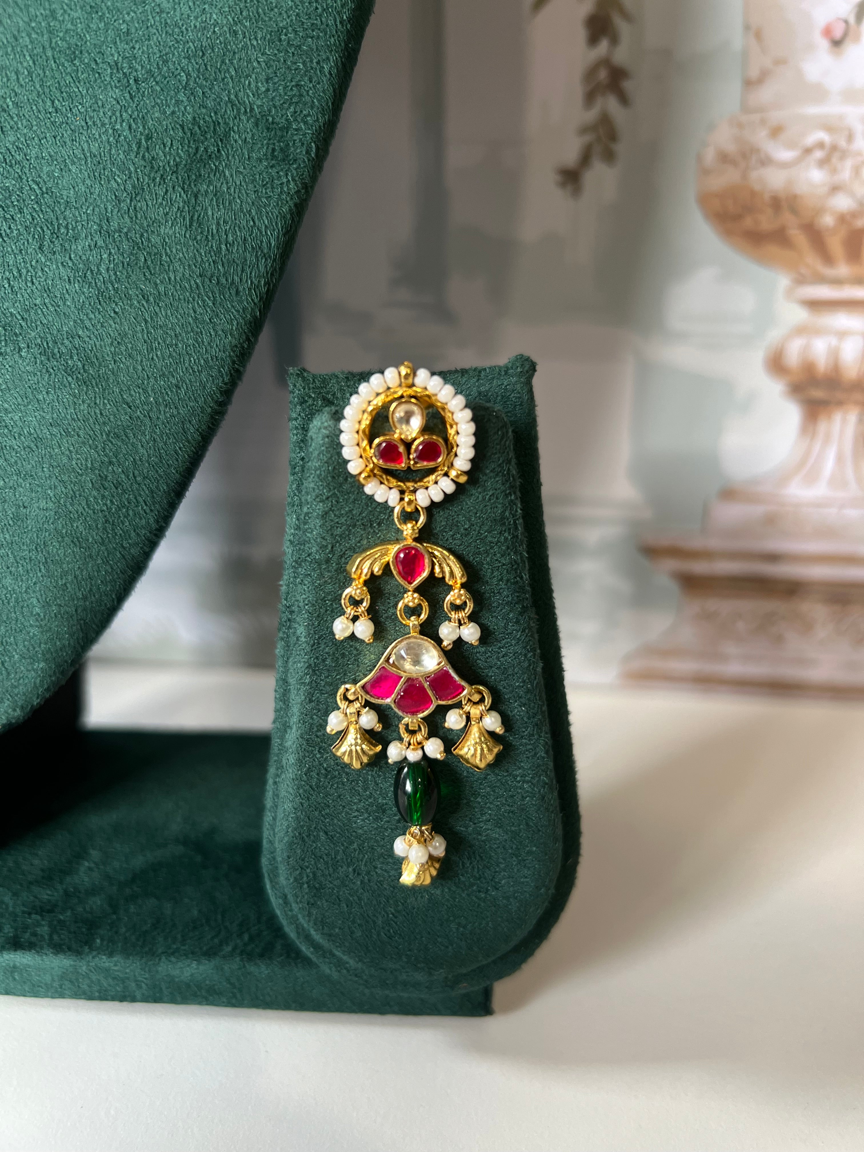 Close-up of matching kundan drop earring with pearl-bordered stud, ruby fan and emerald green bead drop